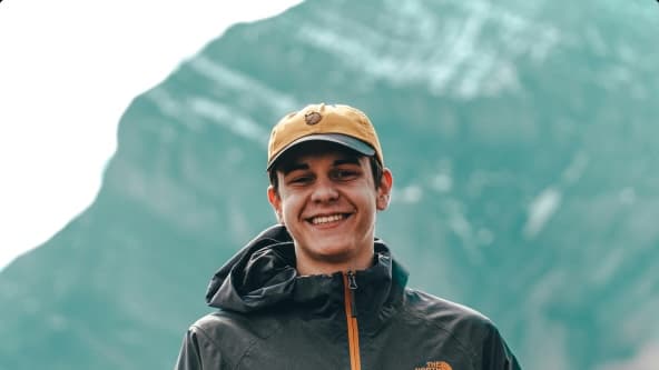 Mies ulkoiluvaatteissa hymyilee kameralle, taustalla vuori.