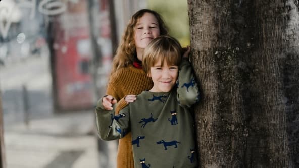 Kaksi lasta katsoo kameraan hymyillen ja halaa toisiaan.